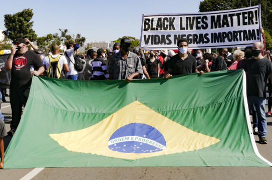 Protesters stand with a Brazilian flag and a sign that reads 