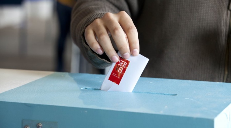 A hand inserting a vote into a ballot box.
