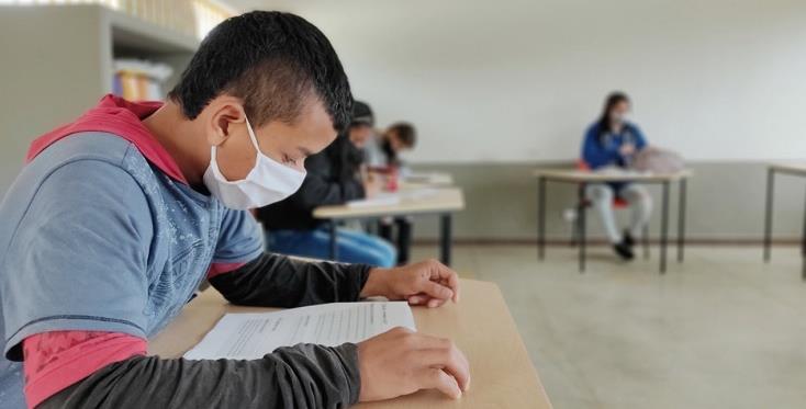A student wearing a mask is reading in a classroom.