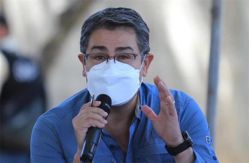 A photo of Honduran President Juan Orlando Hernández talking into a microphone while wearing a surgical face mask.