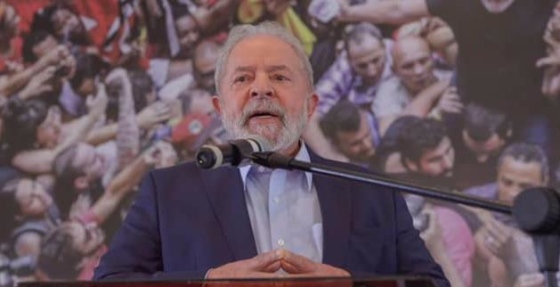 A photo, in color, of former President Luiz Inácio Lula da Silva looking into the camera and speaking into a microphone.